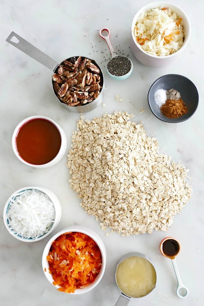 oats, pecans, coconut, carrots, parsnips, honey, and spices in bowls on a countertop