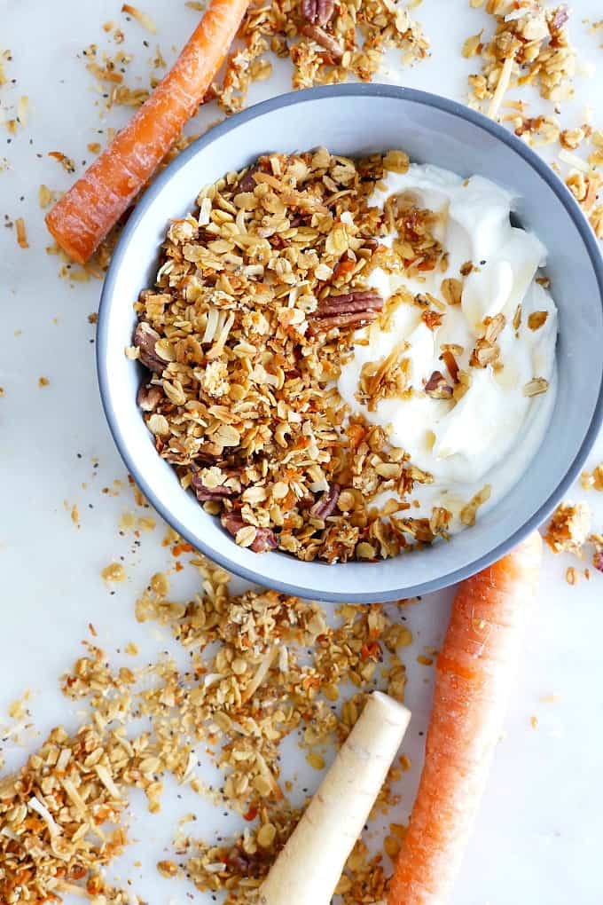 bowl with granola and yogurt surrounded by parsnips, carrots, and granola on a counter