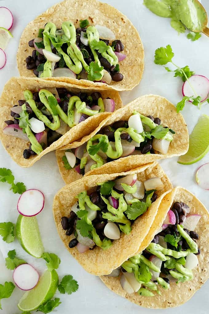 five radish and black bean tacos with avocado crema on a counter