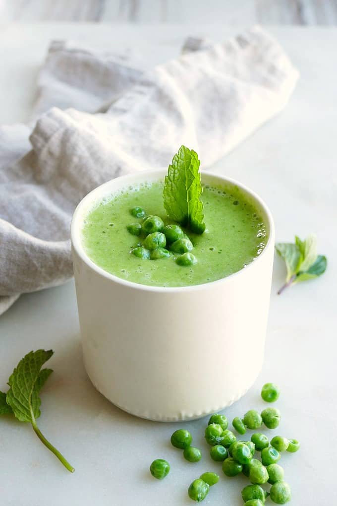green pea and spinach smoothie in a white cup topped with peas and mints