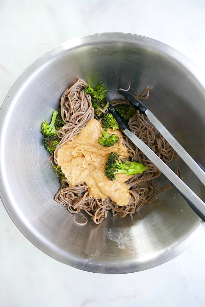 cooked soba noodles, roasted broccoli, and creamy peanut sauce in a mixing bowl