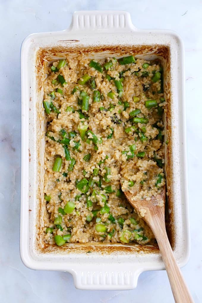 baked brown rice risotto with asparagus in a casserole dish with a spoon on a counter