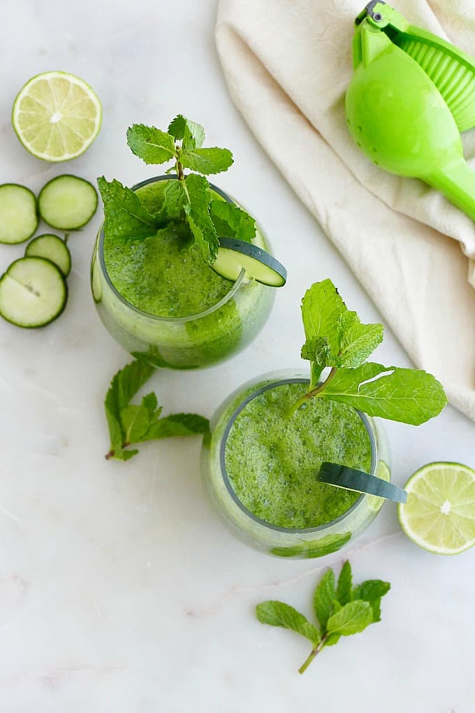 two cucumber gin cocktails garnished with mint leaves and cucumber slices on a counter