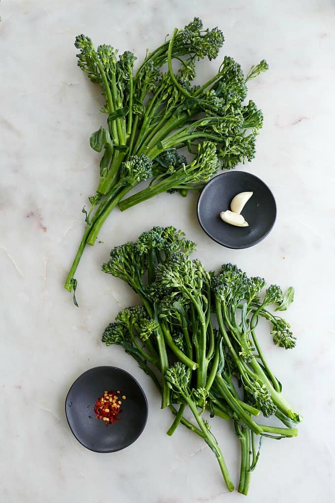 two bunches of broccolini spread out on a counter next to garlic and red pepper