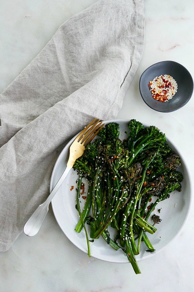 sauteed broccolini on a plate next to a gray napkin and small bowl of seasonings