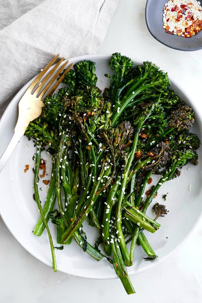 chili sesame broccolini on a white plate with a gold fork