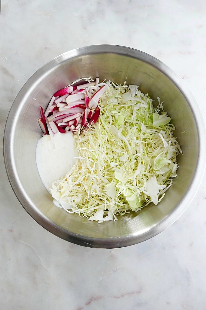 ingredients for coleslaw in a silver mixing bowl on a counter