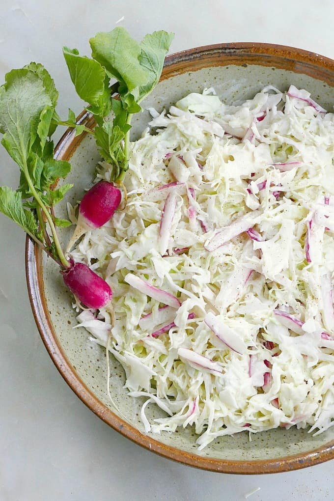 Greek yogurt coleslaw in a bowl with two French breakfast radishes on top