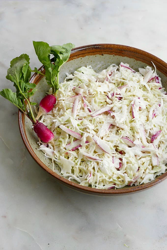 side view of coleslaw in a brown and green bowl with two radishes on top