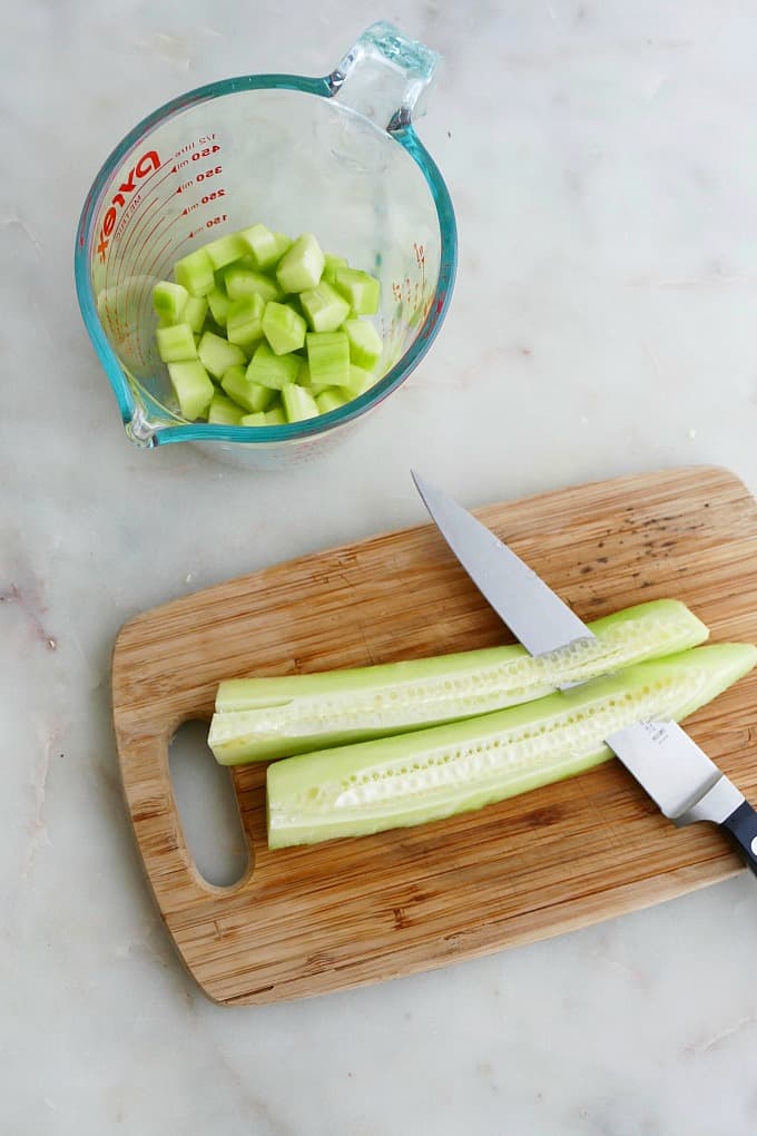 knife slicing the seeds off a cucumber on a bamboo cutting board