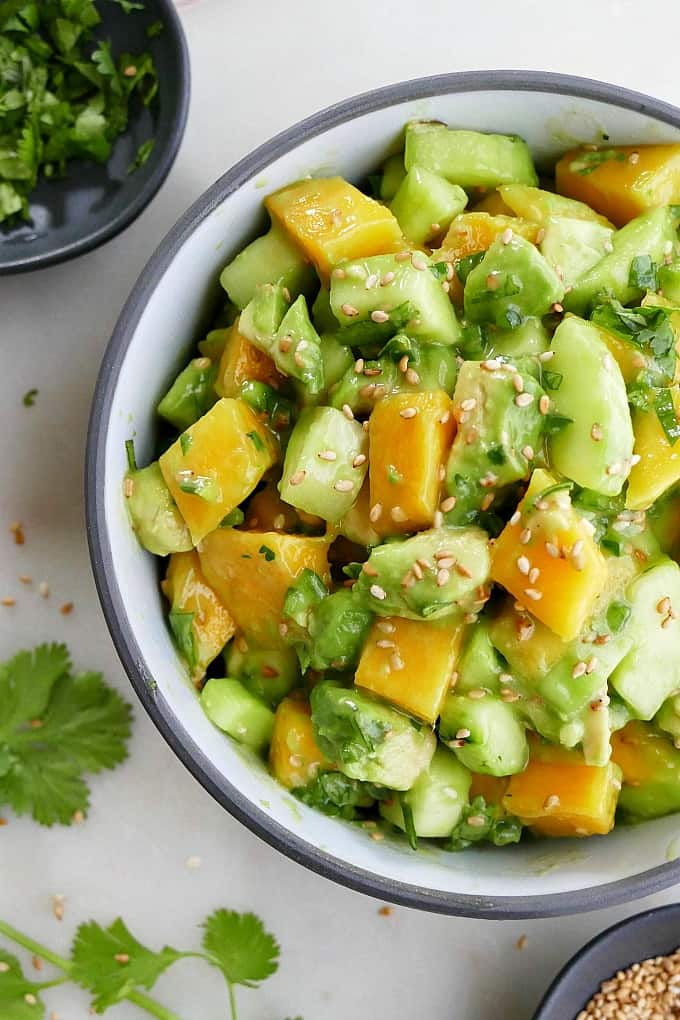 close up of cucumber mango salad recipe in a gray bowl topped with seeds