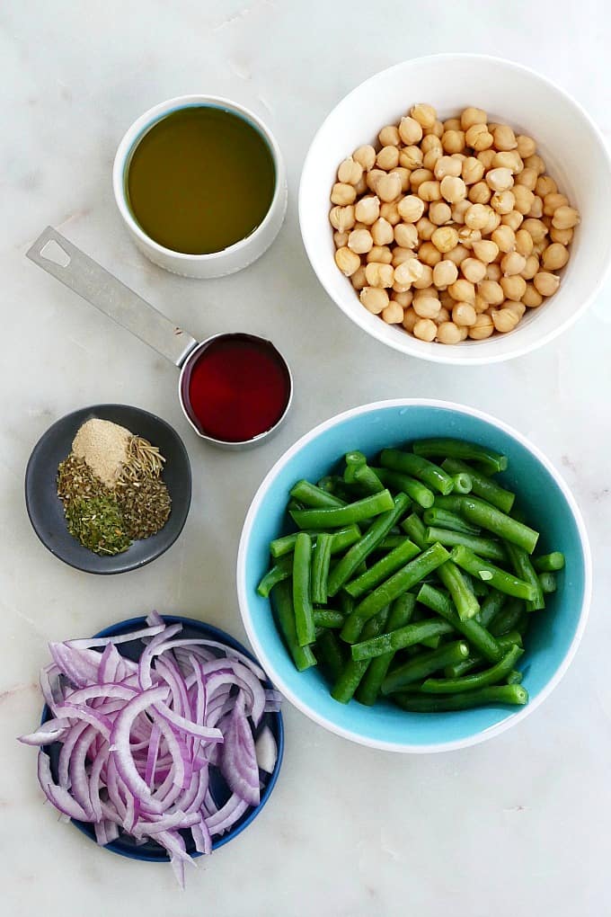 olive oil, chickpeas, red wine vinegar, spices, red onion, and green beans on a counter