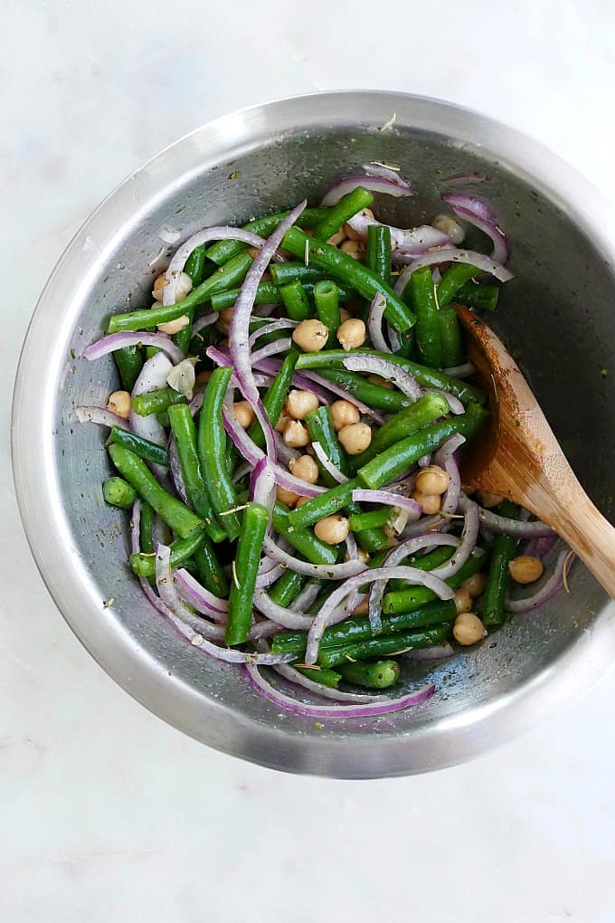 marinated green bean salad ingredients in a mixing bowl with a wooden spoon