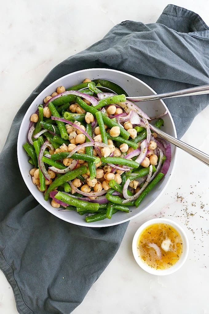 marinated green bean salad in a serving bowl on a napkin next to extra dressing