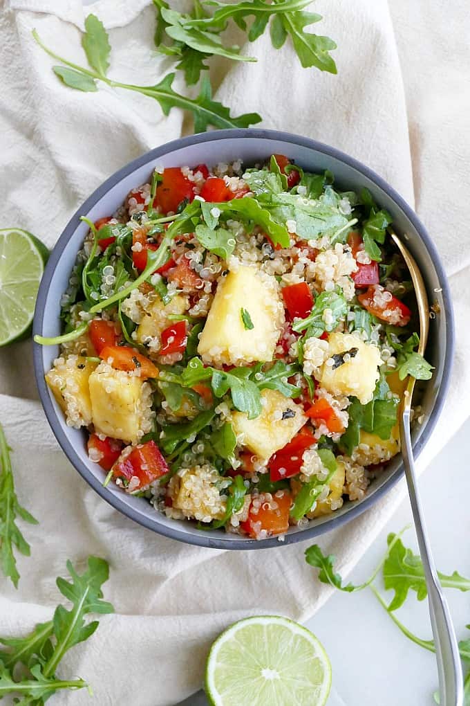 quinoa arugula salad with pineapple in a serving bowl with a spoon