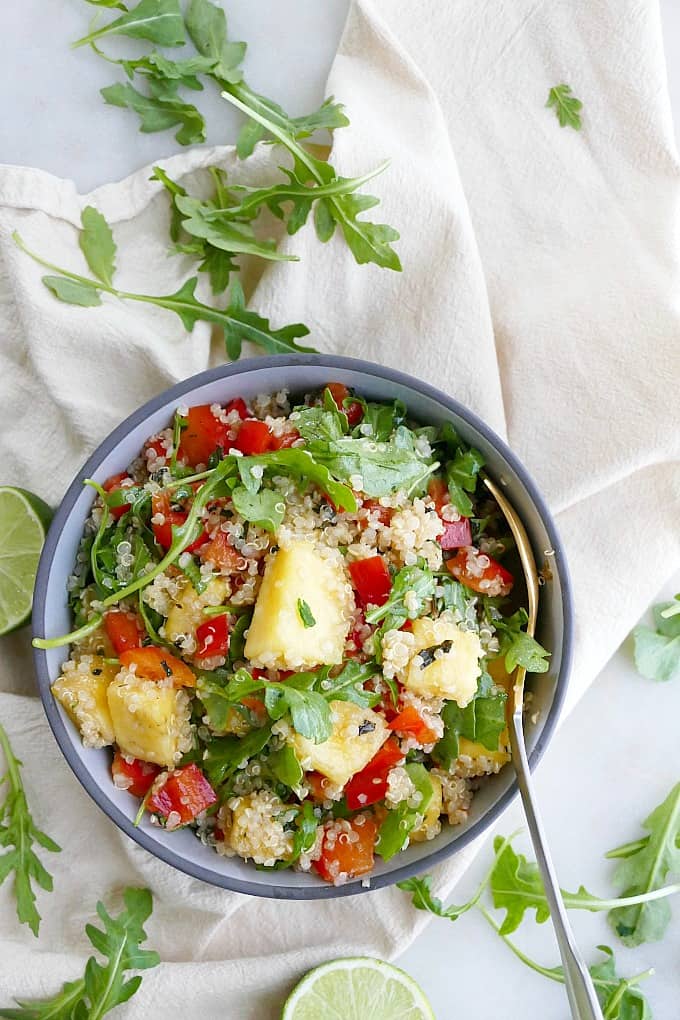 a quinoa salad in a bowl on top of a napkin with arugula leaves around it