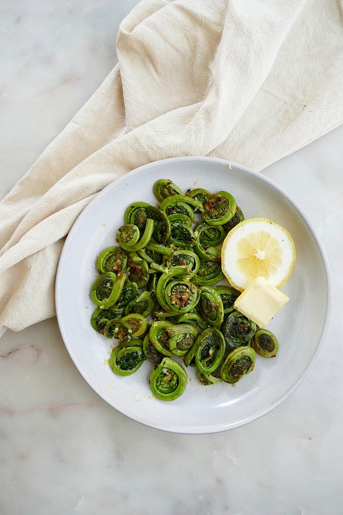 sauteed fiddlehead ferns on a serving plate with butter and lemon