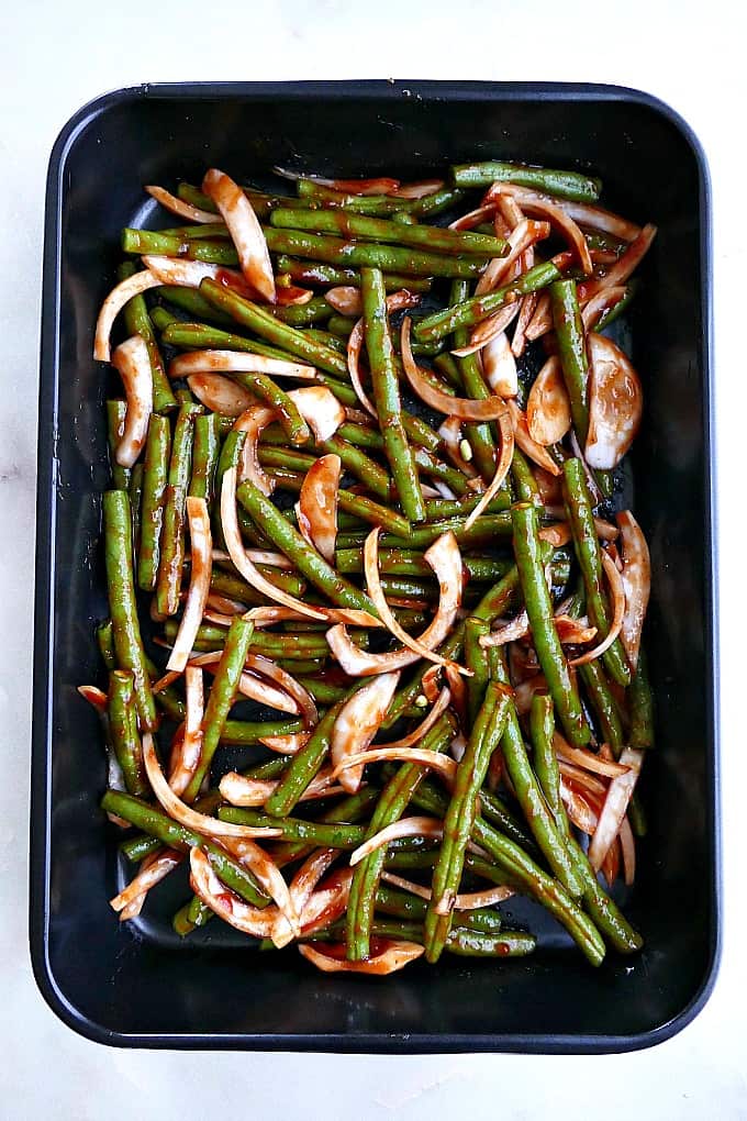barbecue green beans and onions tossed in barbecue sauce in a 9x13 baking dish