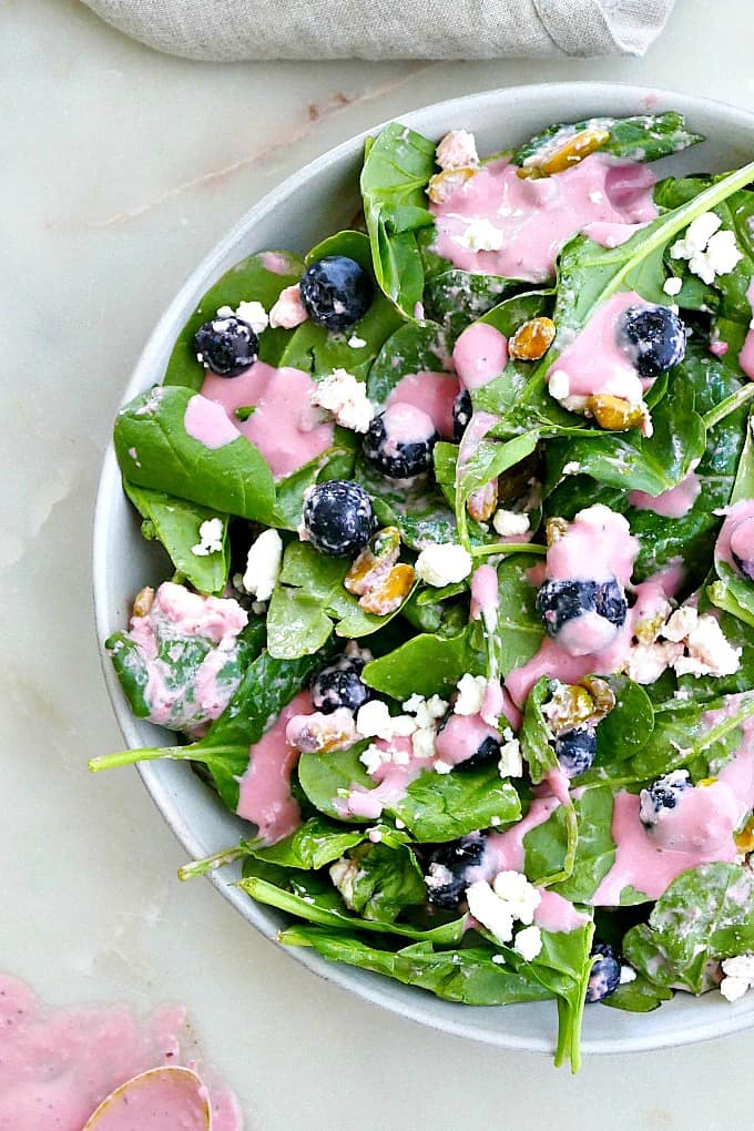 blueberry spinach salad with pink dressing on a white plate on a counter