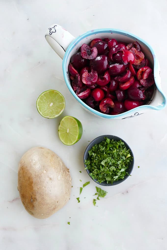 chopped cherries, lime halves, fresh herbs, and jicama spread out on a counter