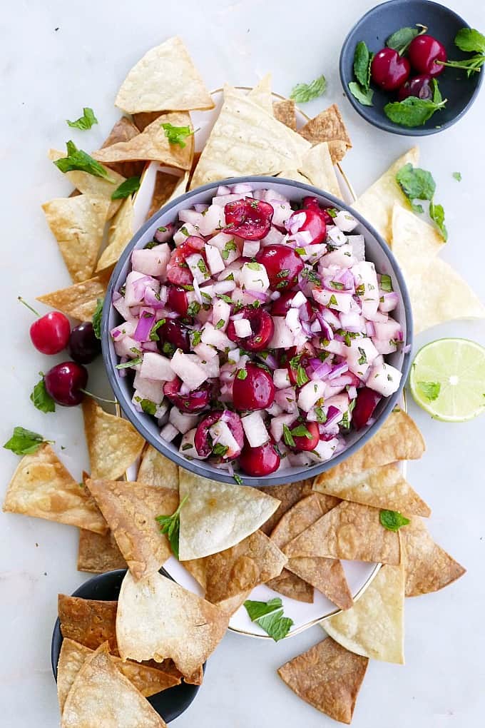 jicama cherry salsa in a serving bowl in the middle of a platter with chips, herbs, and fresh lime