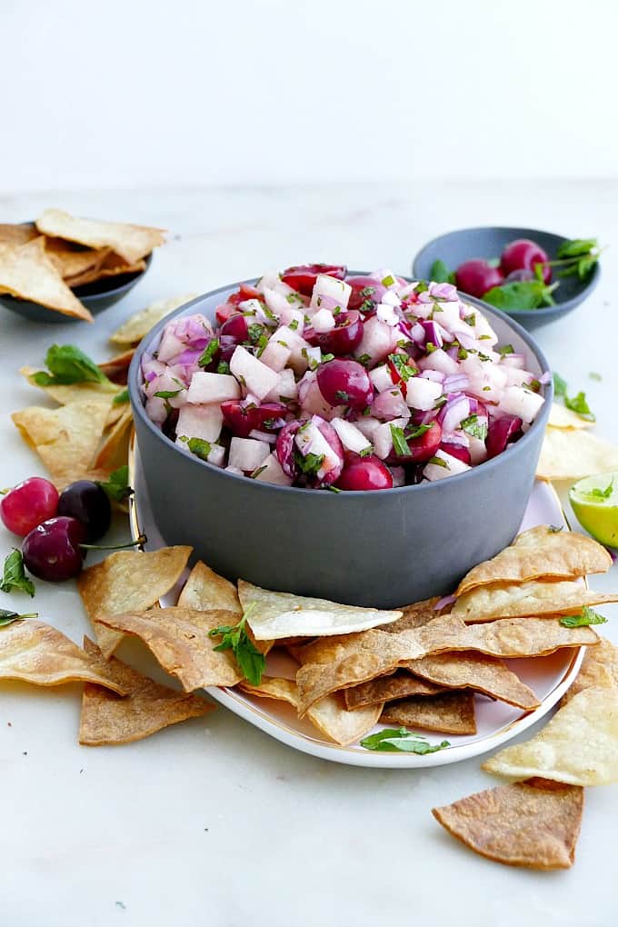 jicama salsa in a grey serving bowl topped with fresh herbs and surrounded by chips