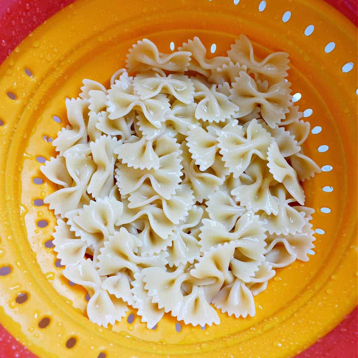 bowtie pasta being drained and rinsed in a colander in the sink