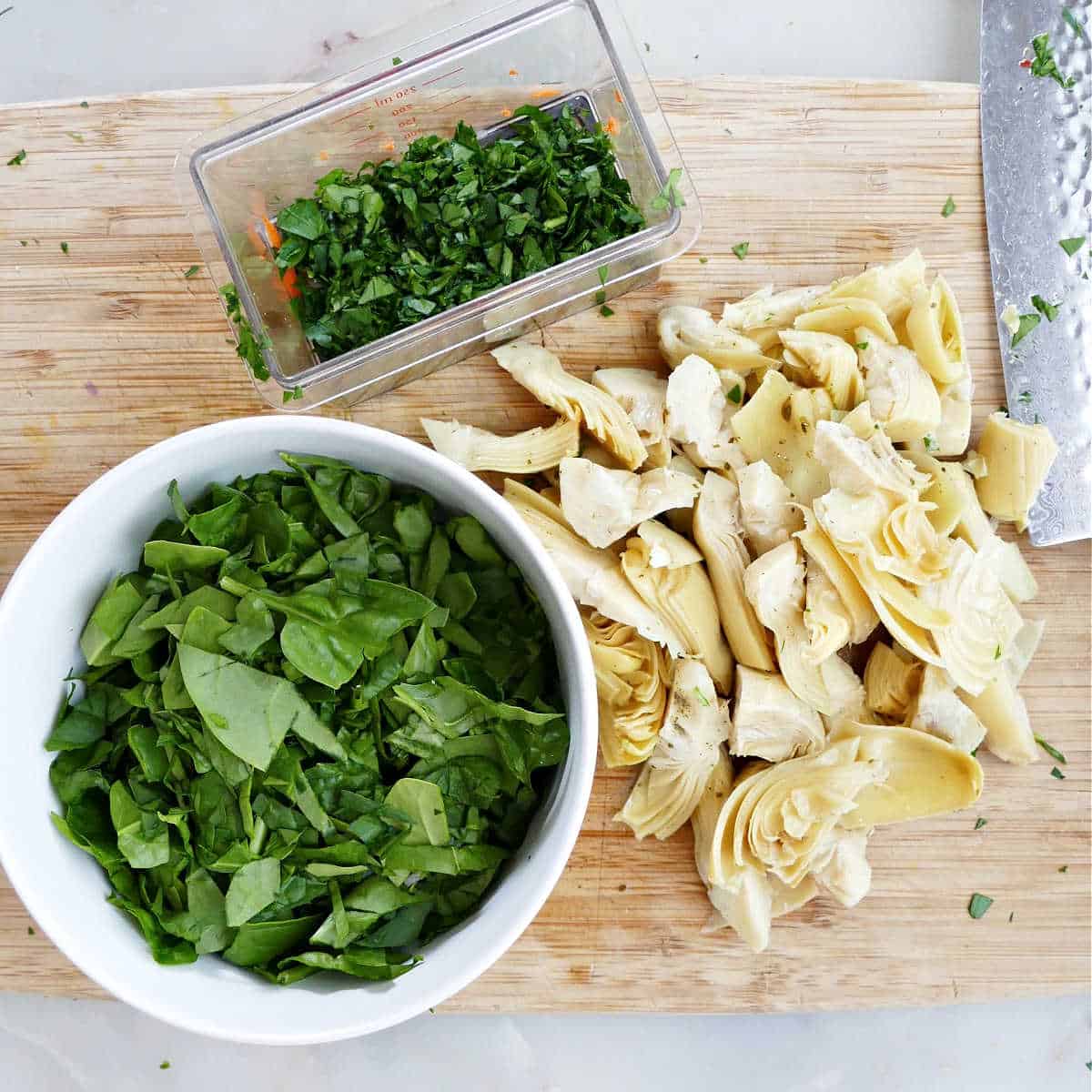 spinach and artichoke hearts being cut up on a cutting board