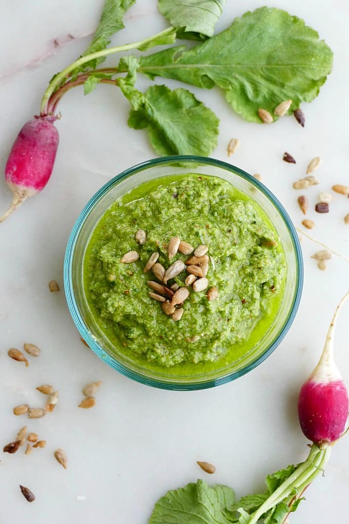 radish top pesto in a glass bowl on a counter topped with sunflower seeds