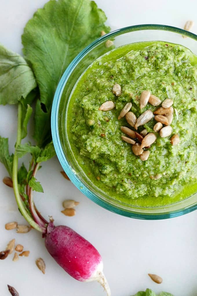 radish top pesto with sunflower seeds on top in a glass container next to a radish