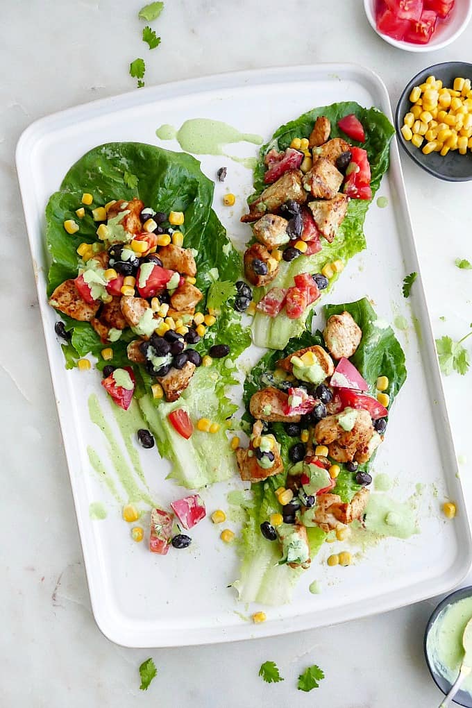 three lettuce chicken wraps on a white platter with veggie toppings and sauce