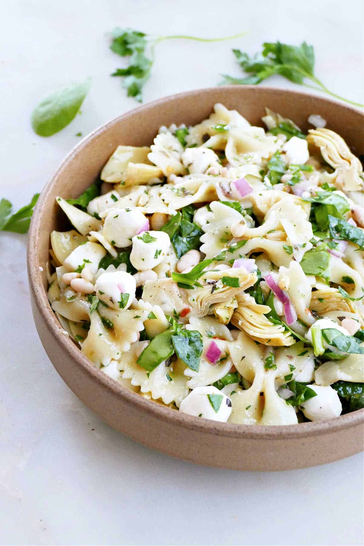 pasta salad ingredients mixed together in a large mixing bowl with a spoon