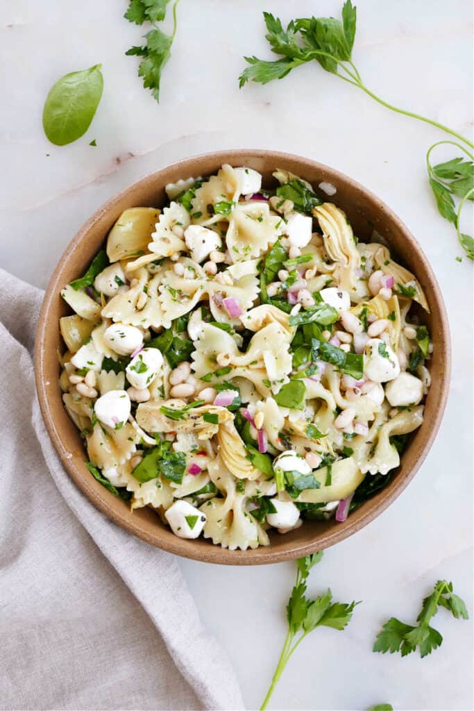 spinach artichoke pasta salad in a serving bowl next to a napkin and parsley