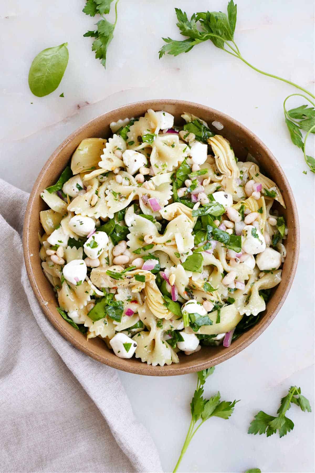 spinach artichoke pasta salad in a serving bowl with a fork