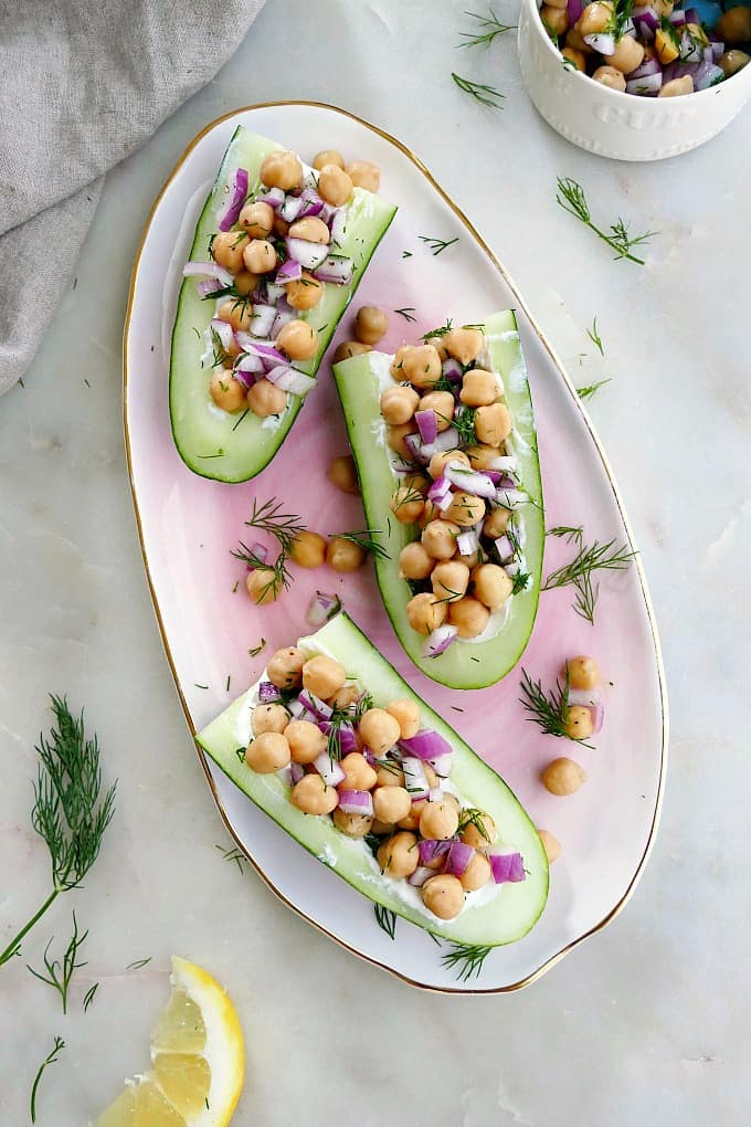 three chickpea salad cucumber boats on a pink platter garnished with herbs