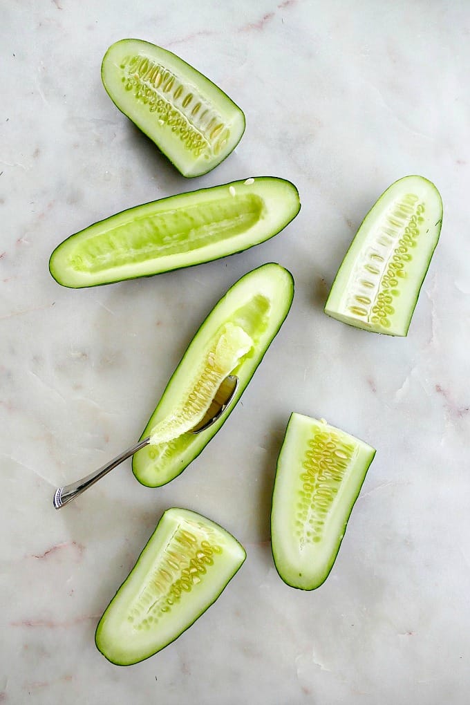 cucumbers sliced in half on a counter with a spoon scooping out seeds from one half