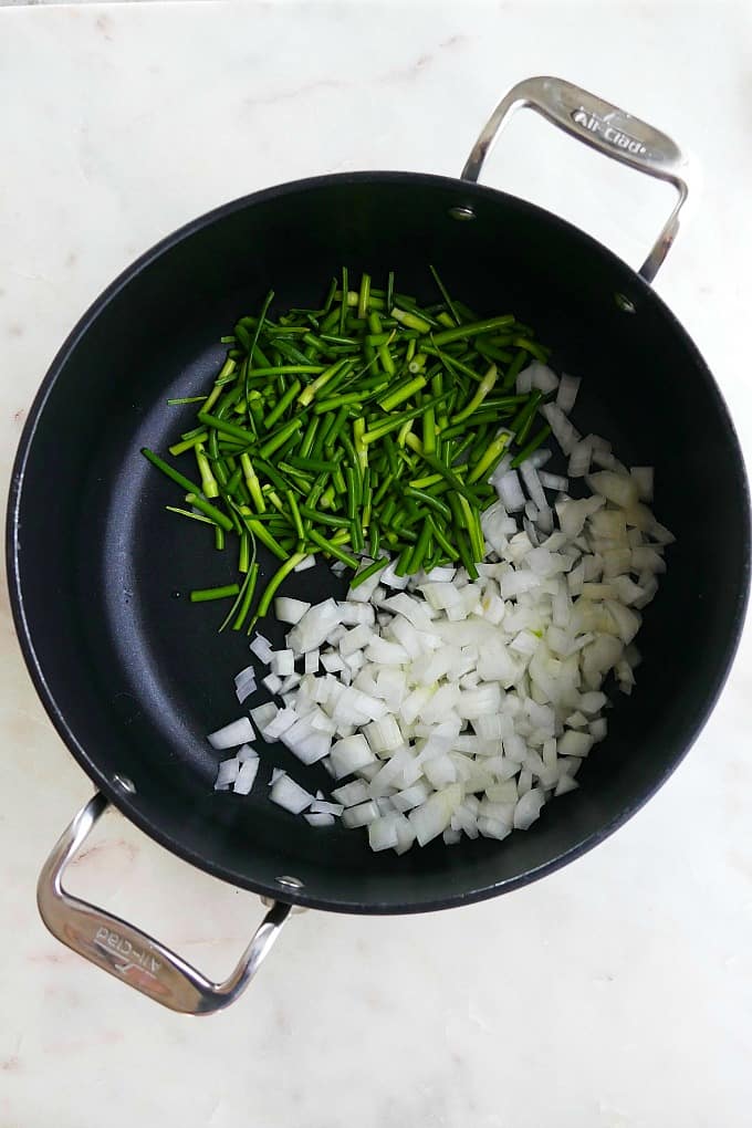 garlic scapes and onion in a pot on a white countertop