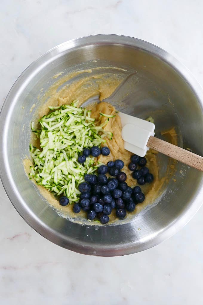 grated zucchini, blueberries, and cookie batter in a mixing bowl with a rubber spatula