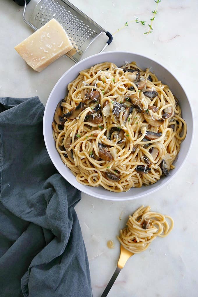 a blue bowl filled with mushroom spaghetti next to a fork and napkin