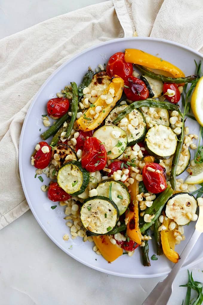 close up of roasted summer vegetables sprinkled with fresh herbs on a plate