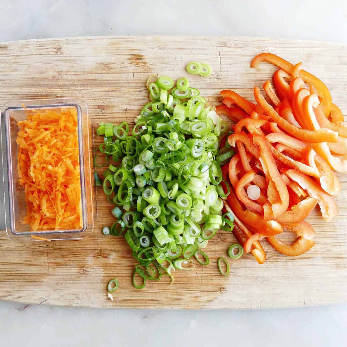 grated carrots, sliced green onions, and sliced bell pepper on a cutting board