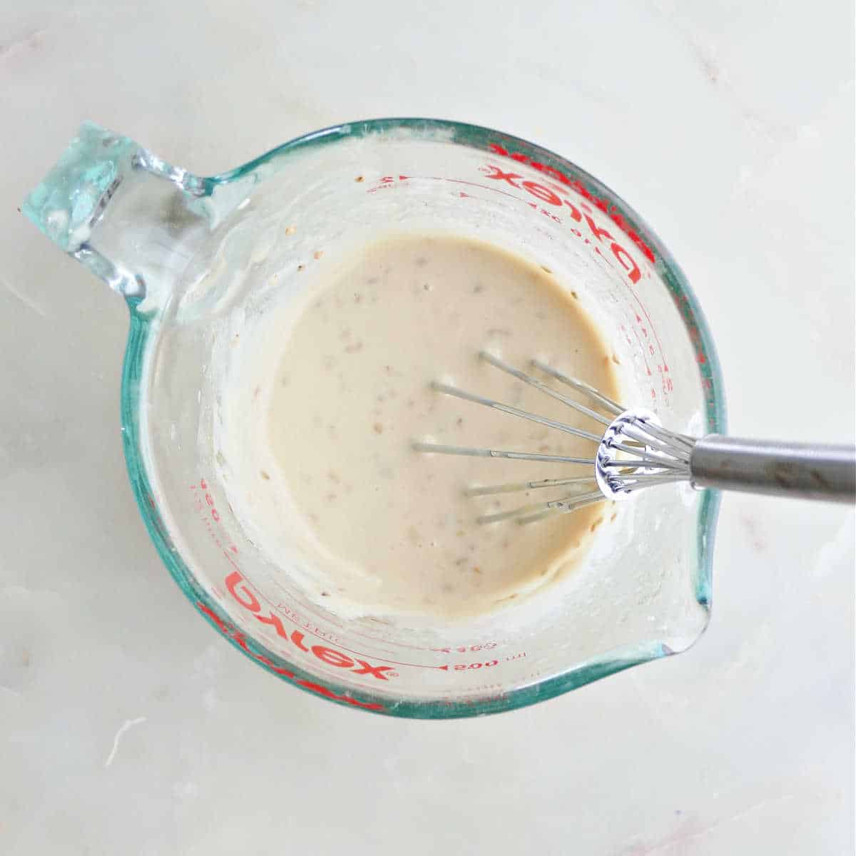 ingredients for lime and tahini dressing whisked together in a measuring cup