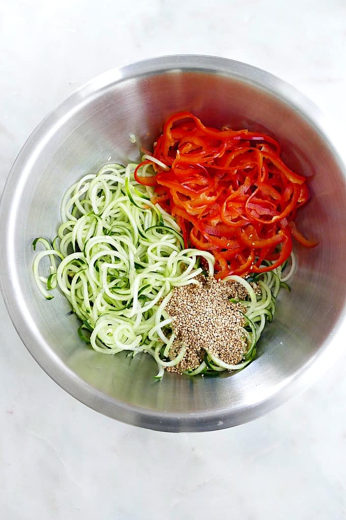 spiralized cucumbers, bell peppers, and toasted sesame seeds in a mixing bowl