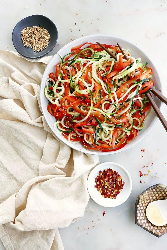 bell pepper and cucumber noodle salad on a white plate with chopsticks next to a napkin