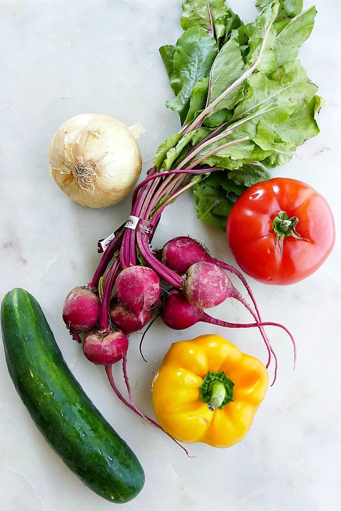 onion, beets, tomato, bell pepper, and cucumber on a white counter