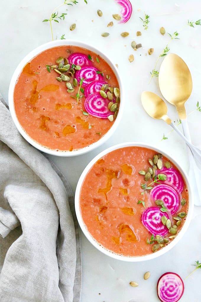 two bowls of cold beet soup with toppings next to spoons and a napkin