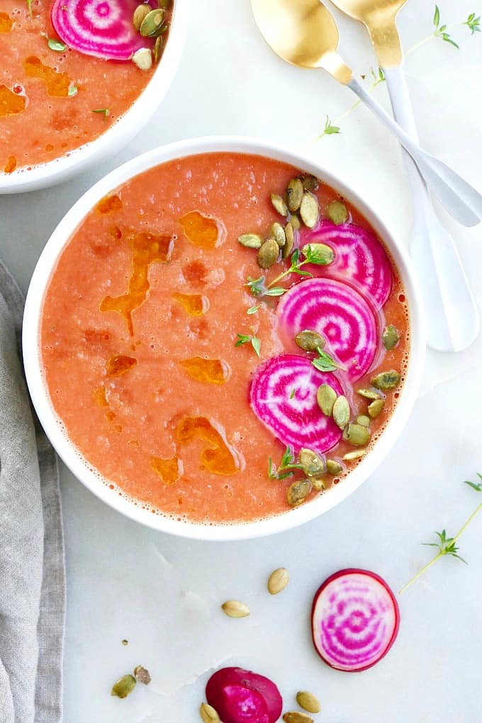 beet gazpacho in a white bowl topped with pink and white beets and seeds