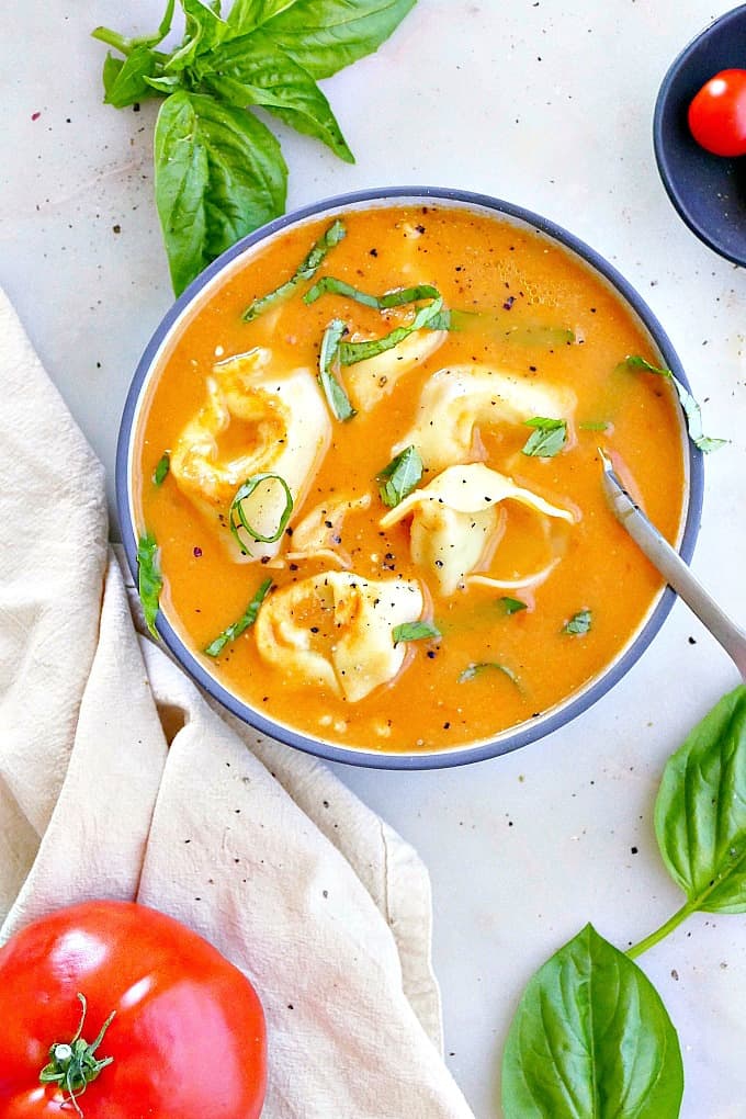 fresh tomato tortellini soup in a blue soup bowl with basil chiffonade