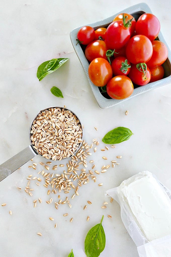 farro, cherry tomatoes, basil leaves, and goat cheese next to each other on a counter