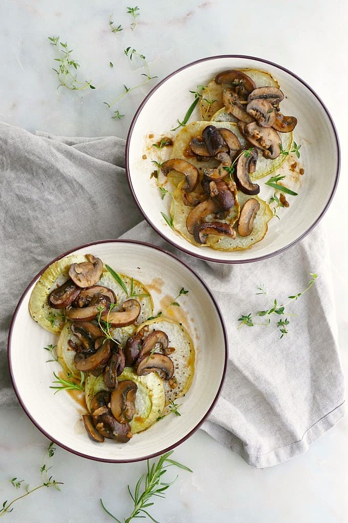 two bowls with kohlrabi steaks with mushroom sauce on a napkin on a counter